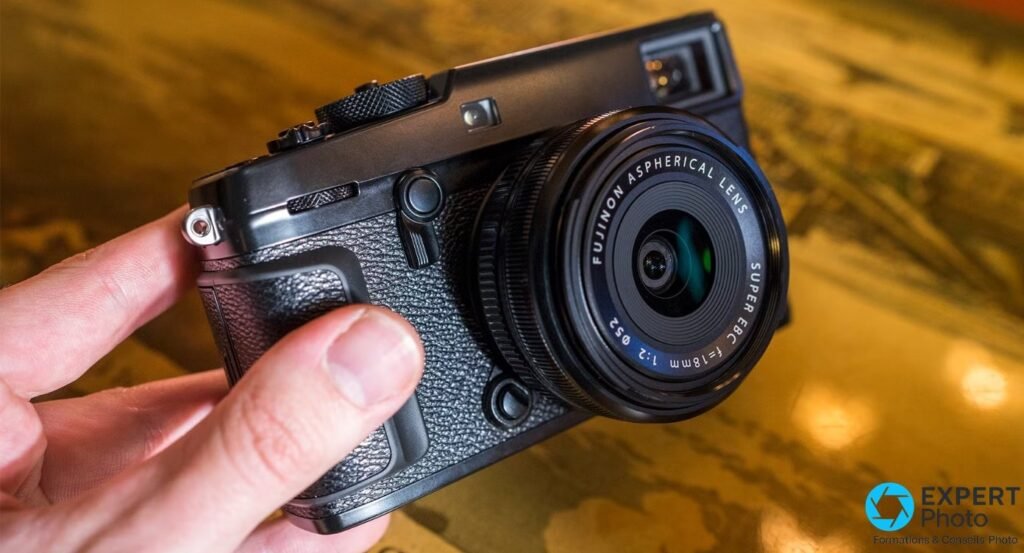 Fujifilm X-Pro2 noir équipé du Fujinon XF 18mm f/2, tenu dans une main, vue trois-quarts avant