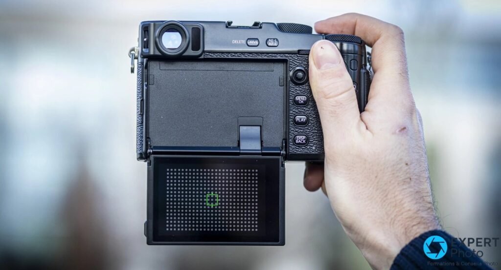 Fujifilm X-Pro3 noir tenu en main, écran principal rabattu vers le bas affichant un motif de points avec carré vert.