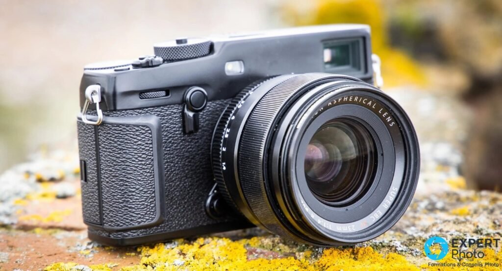 Fujifilm X-Pro3 noir avec Fujinon XF 23mm f/1.4 monté, trois quarts avant gauche, posé sur pierre et lichen jaune.