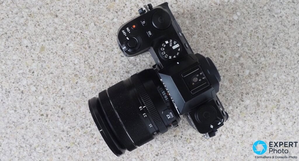 Fujifilm X-S10 vu de dessus en plongée totale, objectif XF 18-55 mm zoom monté, molette PASM et déclencheur visibles.