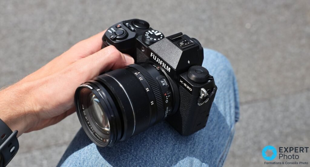 Fujifilm X-S20 tenu en main avec objectif XF 18-55mm f/2.8-4 monté, vue trois quarts avant sur jean bleu