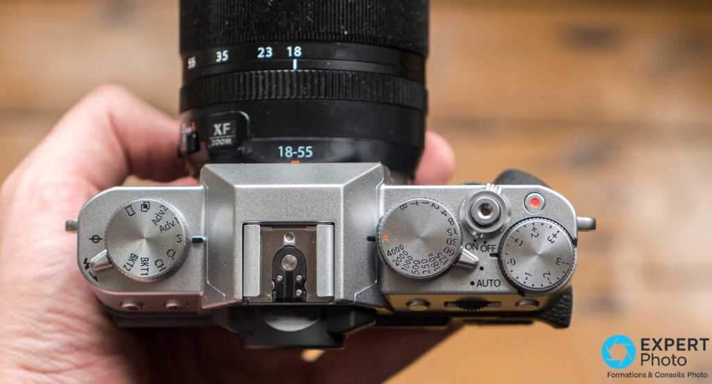 Fujifilm X-T10 vu de dessus, tenu en main : molettes vitesse, correction d'expo et entraînement.