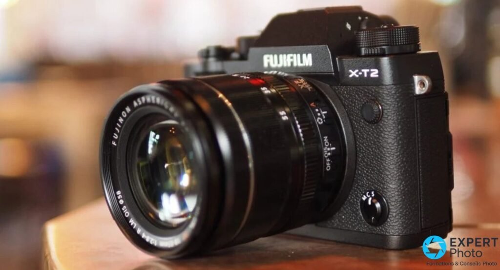 Fujifilm X-T2 avec objectif XF 18-55mm f/2.8-4 R LM OIS, posé sur une table en bois, fond café en bokeh. 