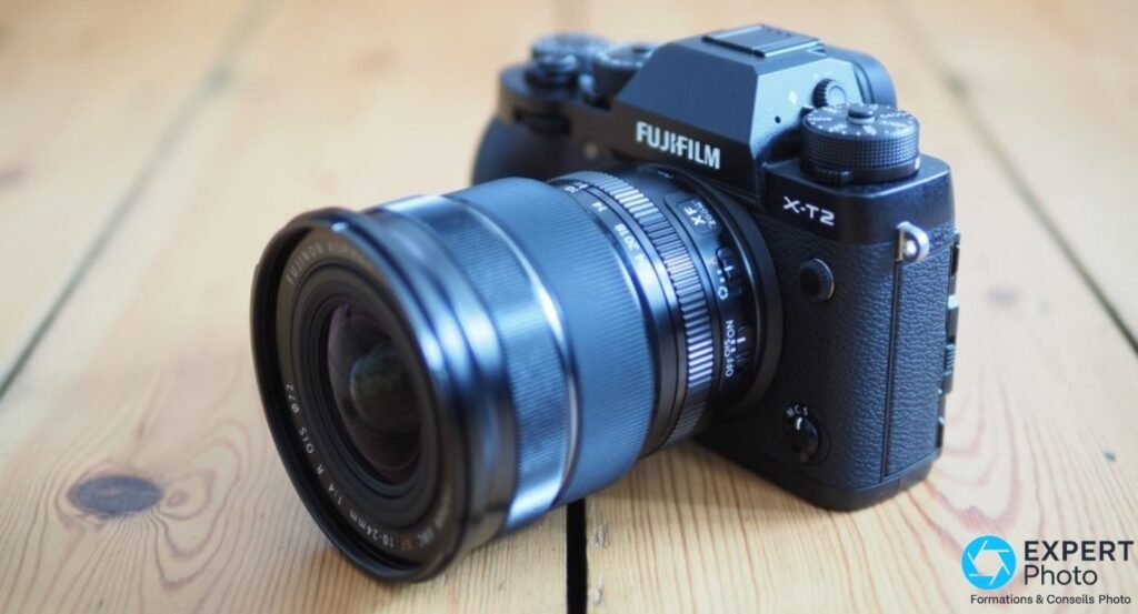 Fujifilm X-T2 équipé d'un objectif grand-angle Fujinon XF 10-24mm f/4 R OIS, posé sur un parquet en bois clair.