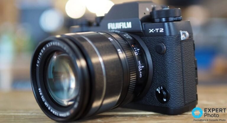 Boîtier hybride Fujifilm X-T2 noir avec objectif XF 18-55mm f/2.8-4 monté, vu trois quarts avant, fond bokeh d'intérieur.