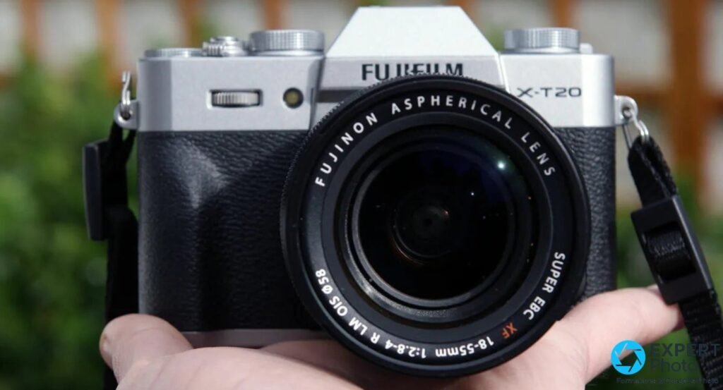 Fujifilm X-T20 argenté monté sur XF 18-55mm tenu en main par un photographe, fond végétal extérieur flou 