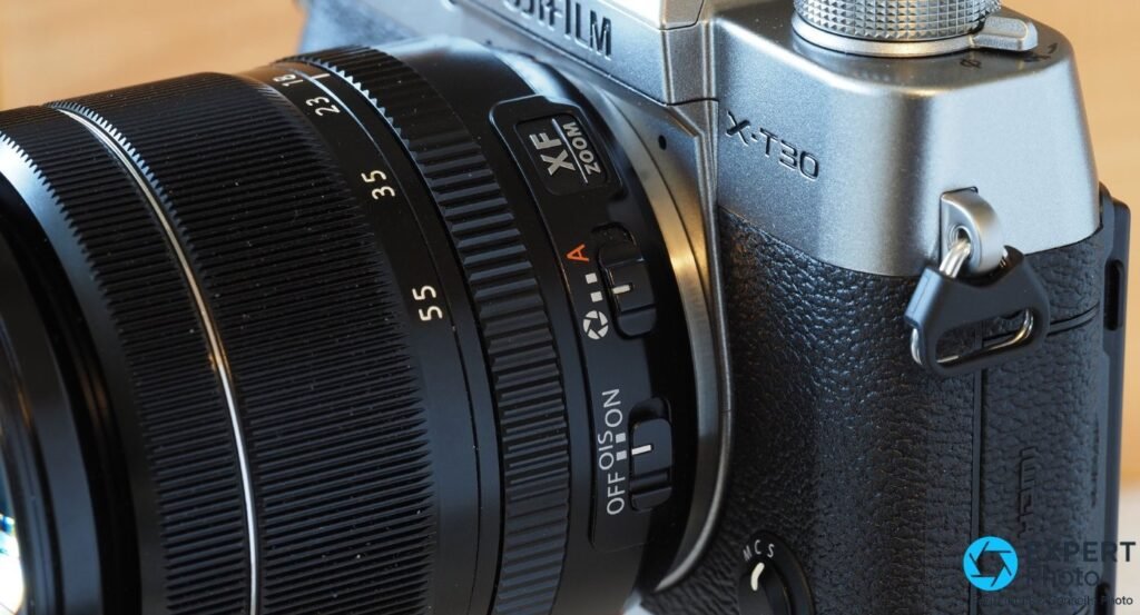 Fujifilm X-T30 II silver, gros plan sur l'objectif Fujinon XF 18-55mm avec bague de zoom et switch OIS.