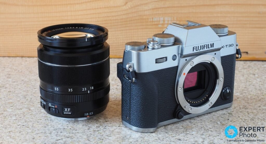 Fujifilm X-T30 II silver et zoom Fujinon XF 18-55mm posés séparément côte à côte sur surface beige.