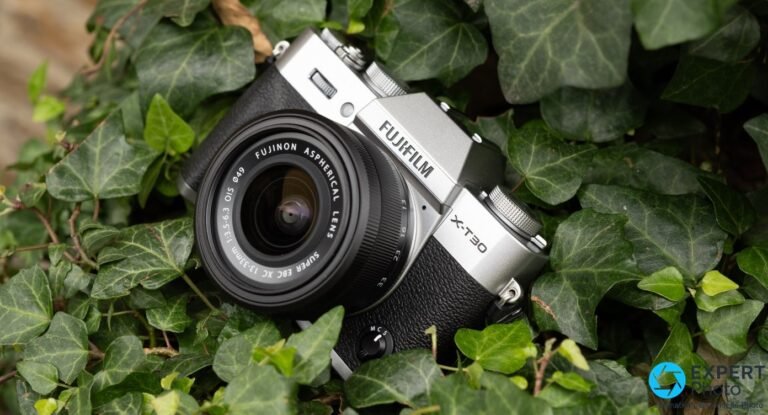 Test Fujifilm X-T30 III : l’hybride APS-C léger pour le voyage et la rue Fujifilm X-T30 III silver avec objectif Fujinon XC 13-33 mm monté, posé sur feuillage de lierre vert, vue 3/4 avant.