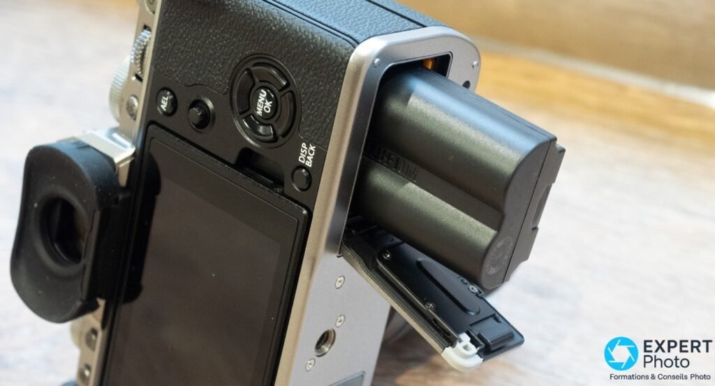 Trappe batterie du Fujifilm X-T4 ouverte avec accumulateur NP-W235 partiellement sorti, slot SD visible.