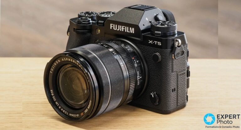 Fujifilm X-T5 noir vu de face en 3/4 avec objectif Fujinon XF 18-55 mm f/2.8-4 R LM OIS sur table en bois.