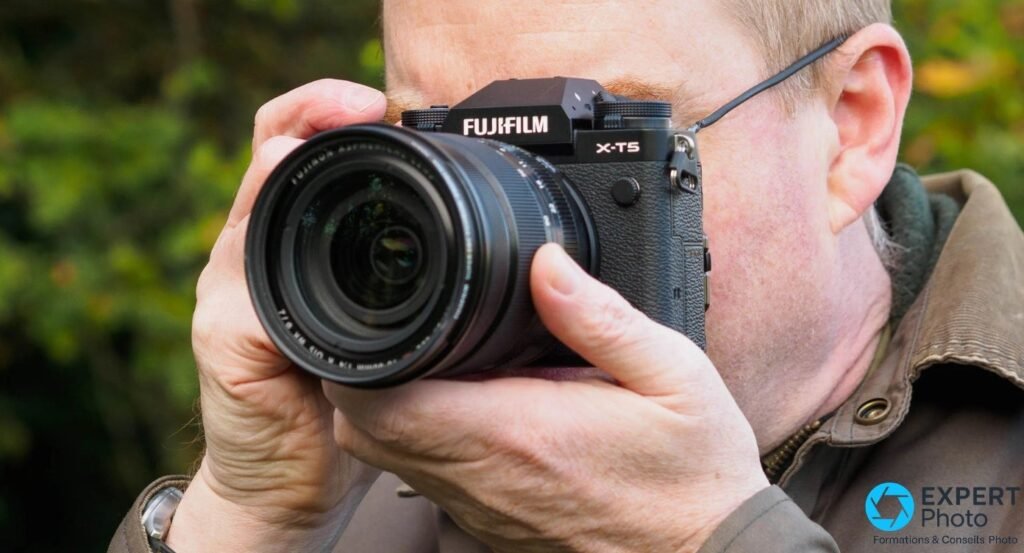 Photographe utilisant le Fujifilm X-T5 en extérieur, œil collé au viseur EVF, fond verdoyant flou.