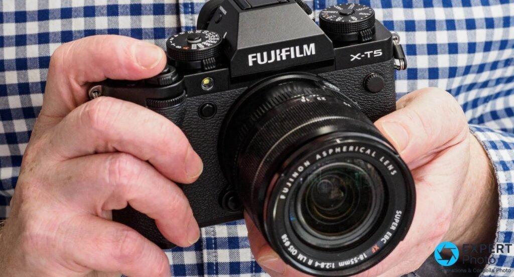 Fujifilm X-T5 tenu à deux mains, vue de face avec objectif Fujinon XF 18-55 mm, prise en main réelle. 