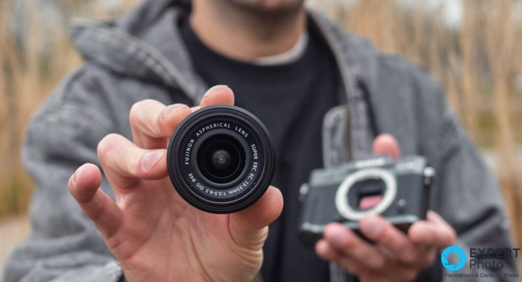 Optique Fujinon XC 13-33mm du kit Fujifilm X-T30 III tenue de face en extérieur, boîtier sombre flou en arrière-plan.