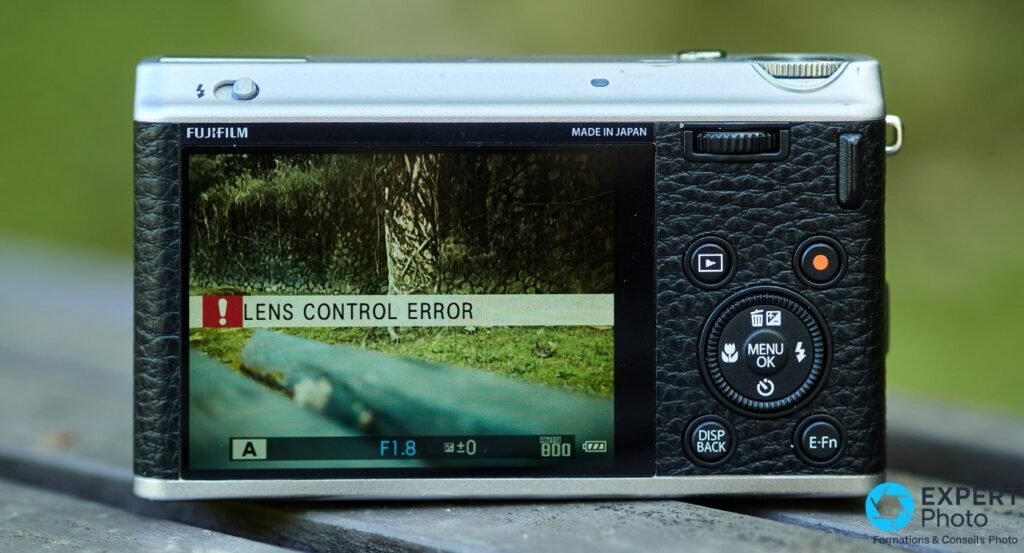 Fujifilm XF1 vu de dos, écran affichant le message d'erreur Lens Control Error sur fond de banc en bois 