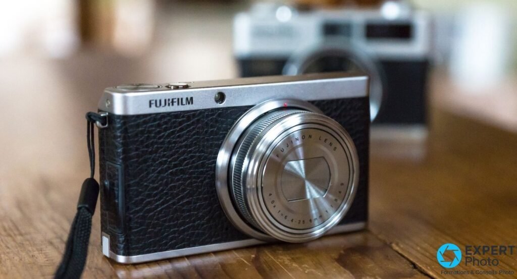 Fujifilm XF1 noir et argenté vu de 3/4 avant, optique rétractée, posé sur une table en bois sombre
