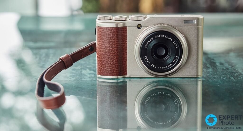Fujifilm XF10 champagne vu de face, dragonne cuir marron repliée, posé sur surface verre turquoise avec reflet
