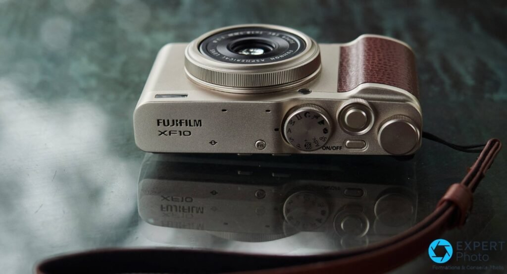 Fujifilm XF10 en trois quarts dessus, capot avec FUJIFILM XF10 et molette des modes, objectif Fujinon sorti