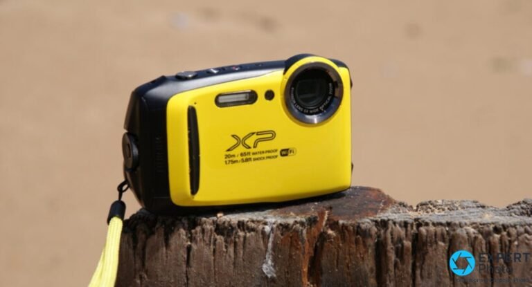 Fujifilm XP130 jaune posé sur une souche de bois, dragonne jaune pendante, plage de sable floue en arrière-plan