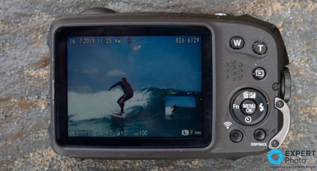 Fujifilm XP140 vu de dos, écran allumé affichant une photo de surfeur, boutons W, T, MENU et croix de navigation.