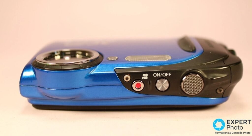 Tranche supérieure du Fujifilm XP70 montrant le déclencheur cranté, le bouton ON/OFF et la touche vidéo rouge