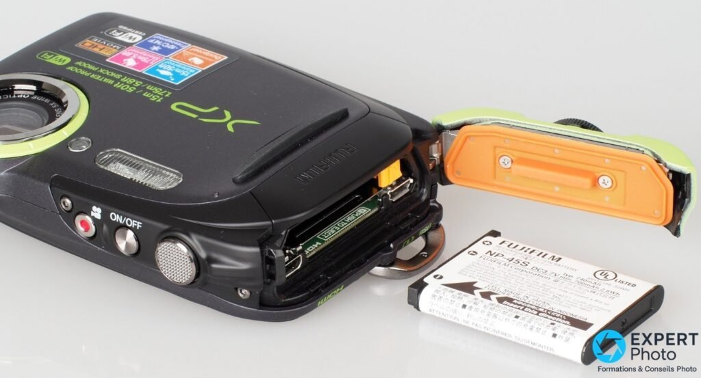 Trappe latérale ouverte du Fujifilm XP80 montrant carte SD, port HDMI et batterie NP-45S 740 mAh posée à côté.