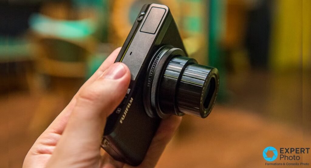 Fujifilm XQ1 vu de trois quarts dessus, objectif Fujinon déployé en position zoom, marquage ASPHERICAL LENS lisible.