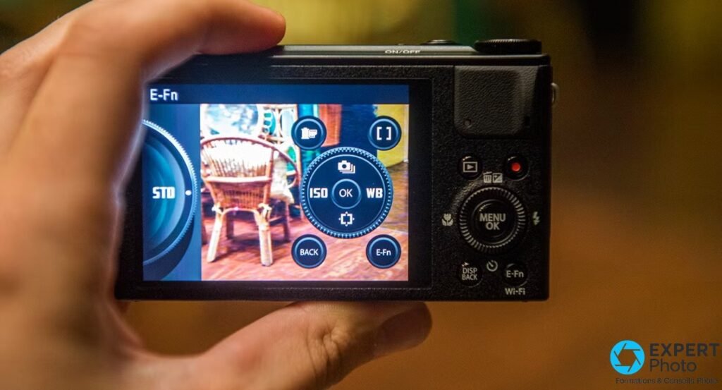 Fujifilm XQ1 vu de dos, écran LCD allumé sur le menu E-Fn, boutons MENU/OK, DISP BACK et Wi-Fi visibles, tenu en main.