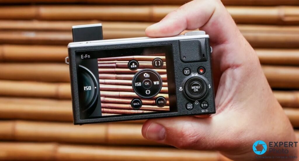 Fujifilm XQ2 vu de dos, écran arrière allumé affichant le menu E-Fn (ISO, OK, WB), tenu en main droite.