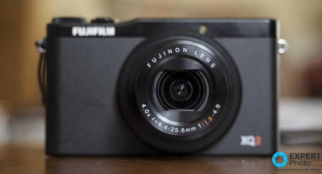 Fujifilm XQ2 noir vu de face, objectif Fujinon LENS déployé, marquage 4.0x f=6.4-25.6mm 1:1.8-4.9 lisible.