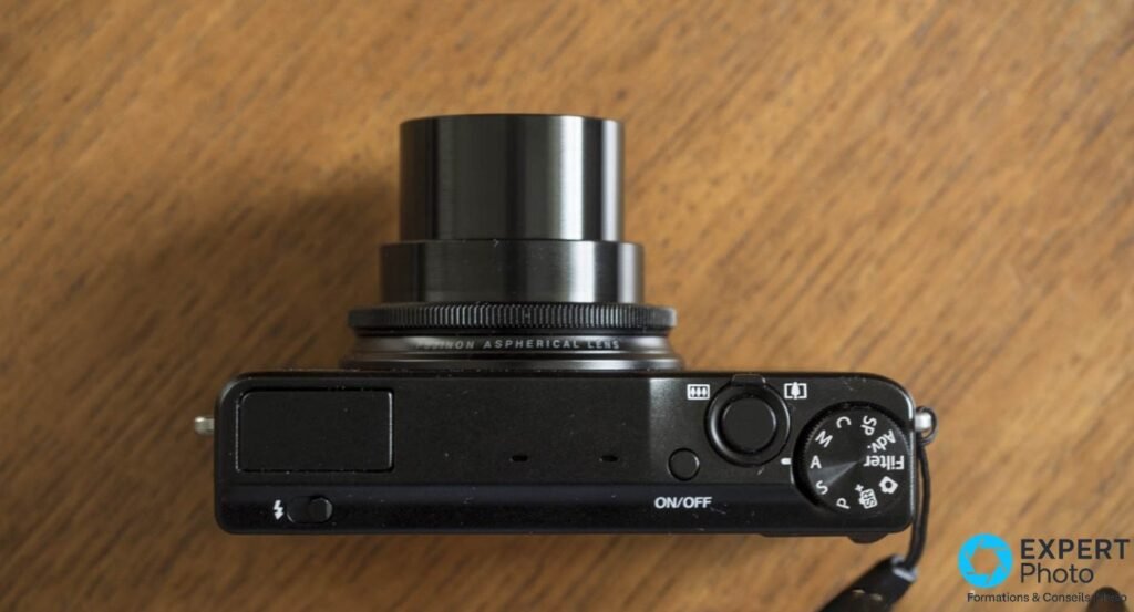 Fujifilm XQ2 noir vu de dessus, objectif Fujinon Aspherical Lens déployé, bague de contrôle visible.