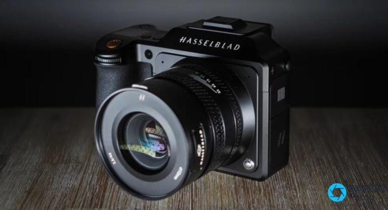 Hasselblad X2D 100C vu de trois quarts avant, équipé d'un objectif XCD, posé sur bois.
