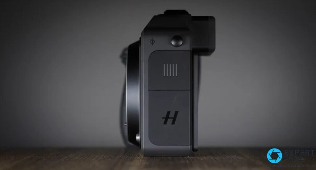 Profil du Hasselblad X2D II 100C avec trappe laterale gravee du logo H et un bouton sur le dessus, sur fond gris. 