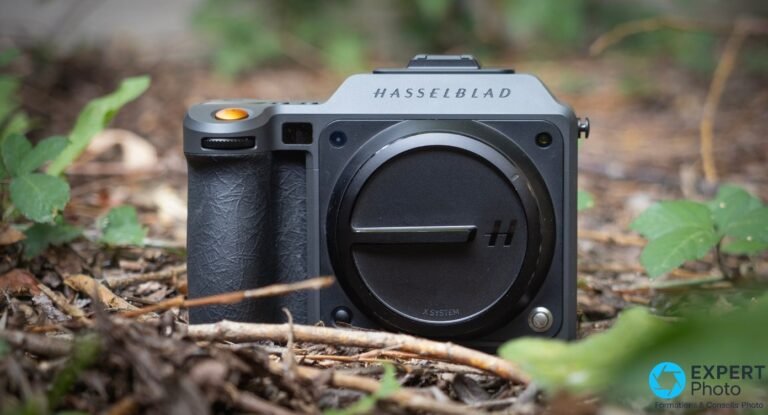 Hasselblad X2D II 100C de trois quarts avant pose au sol, bouchon de boitier monte, poignee et declencheur orange visibles.