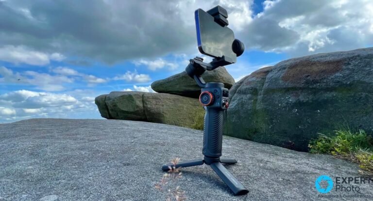 Hohem iSteady M6 Kit : avis 2026 sur le gimbal IA pour créateurs solo Gimbal Hohem iSteady M6 Kit sur trépied déployé, smartphone monté en haut, posé sur un rocher, ciel nuageux