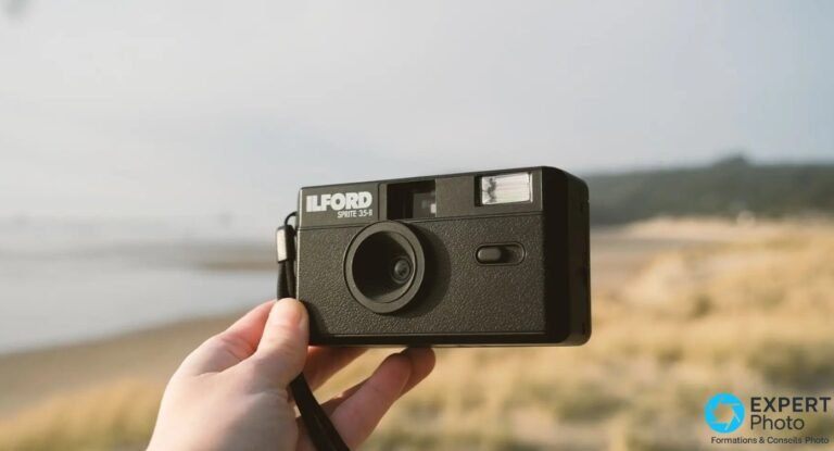 Ilford Sprite 35-II noir tenu par une main, marquage ILFORD SPRITE 35-II lisible, plage et dune floues derrière