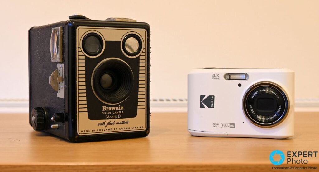 Kodak Pixpro FZ45 blanc de face à côté d'un ancien Kodak Brownie Six-20 Model D noir, sur un plan en bois