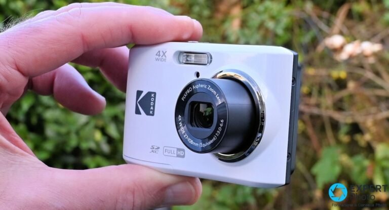 Test Kodak Pixpro FZ45 : ce que vaut vraiment ce compact à petit prix Kodak Pixpro FZ45 blanc de face tenu en main, objectif 4X Wide PIXPRO déployé, fond végétal flou