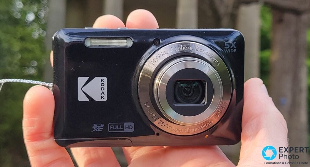 Compact Kodak Pixpro FZ55 noir tenu en main, logo Kodak, objectif PIXPRO 5x 28-140 mm déployé, mentions SDXC et Full HD