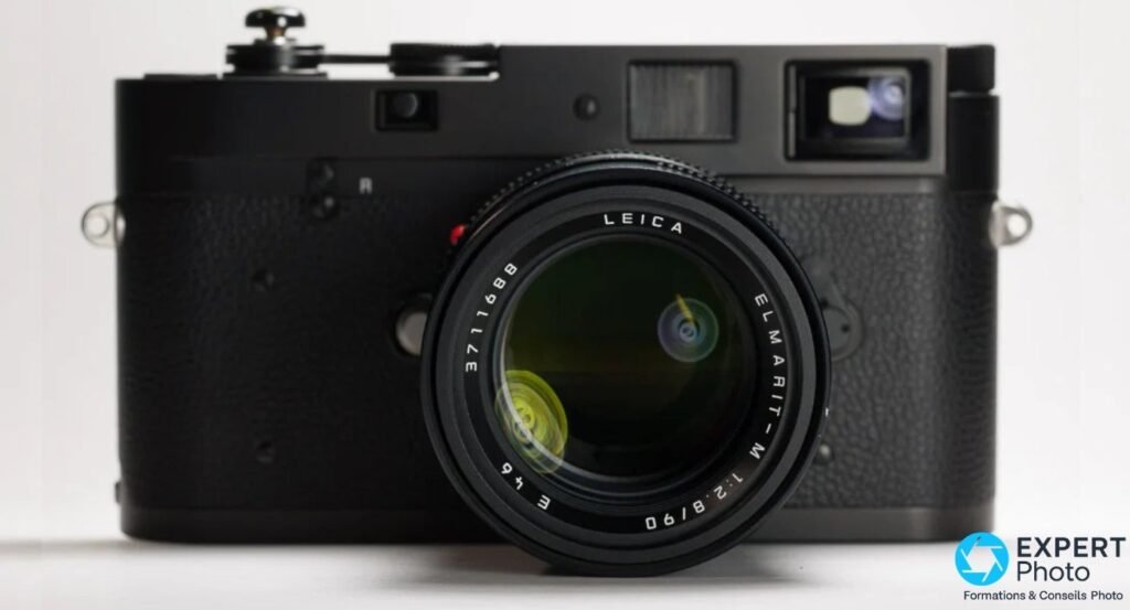 Boîtier Leica M-A noir de face équipé d'un objectif Leica Elmarit-M 90 mm f/2,8, sur fond blanc
