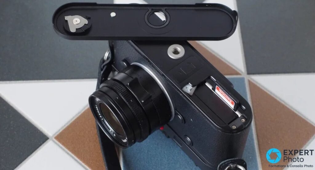 Leica M10 Monochrom vu du dessous, semelle détachée, logement carte SD ouvert avec carte SanDisk insérée.