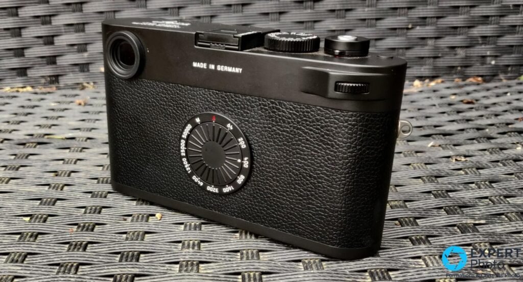 Boîtier Leica M11-D tenu en main, vu en trois-quarts arrière, molette ISO crantée et dos lisse sans écran. 