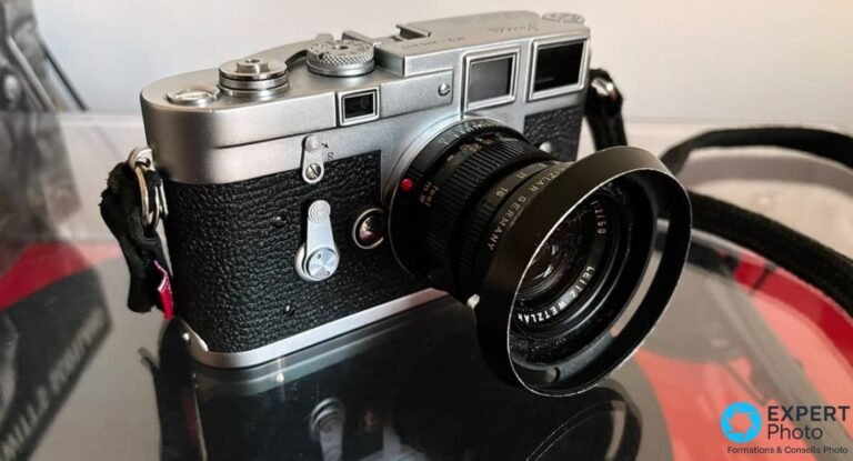 Leica M3 de trois quarts avant, objectif noir Leitz Wetzlar 50 mm f/2 et pare-soleil ajoure, sur surface noire.