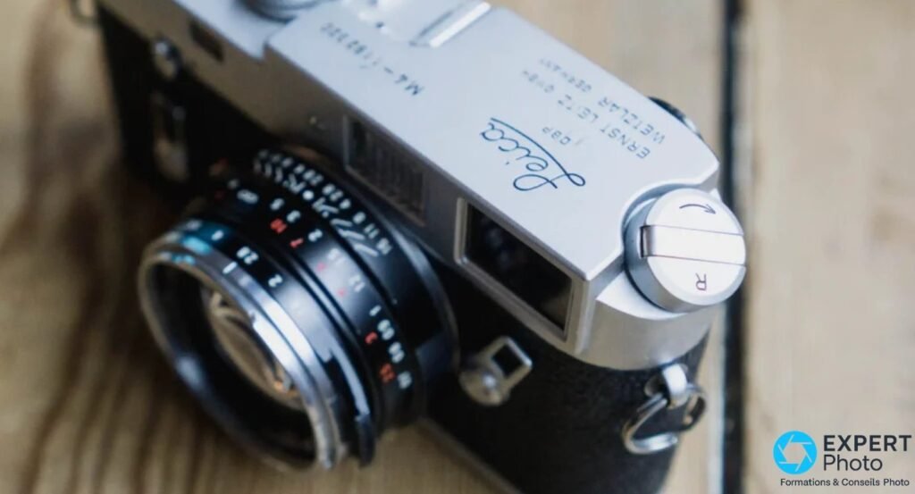 Leica M4 de trois quarts, deux fenêtres du viseur télémétrique, objectif noir avec bagues de réglage, sur bois. 