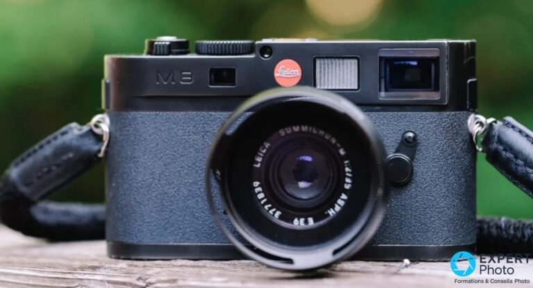 Leica M8 : avis et conditions d’un achat d’occasion Face avant d'un Leica M8 gris-noir, objectif Leica Summilux-M et pare-soleil rond, posé sur bois, fond vert flou.