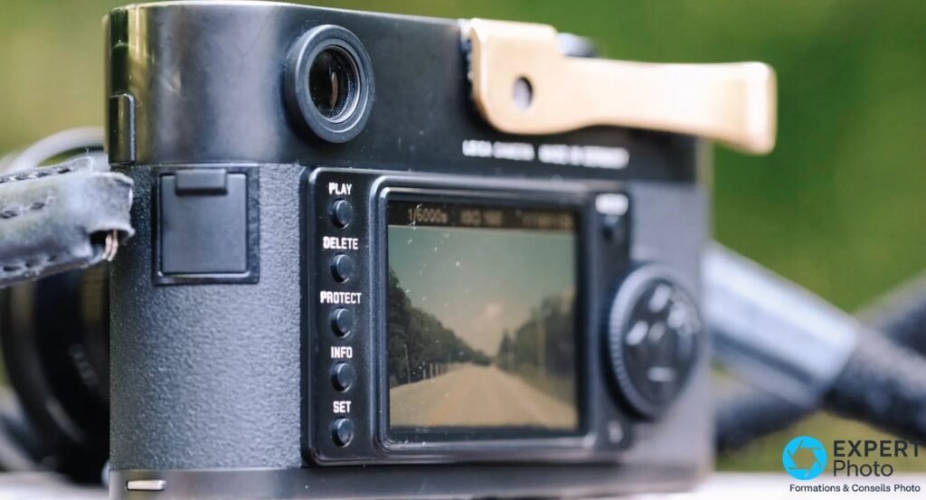 Leica M8 de trois quarts arrière, écran faiblement allumé, touches PLAY DELETE PROTECT INFO SET et repose-pouce doré.