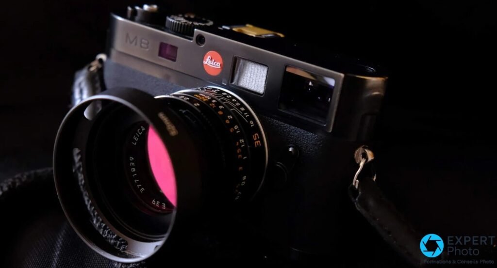 Leica M8 noir de trois quarts sur fond noir, objectif 35 mm monté et reflet magenta sur la lentille frontale.