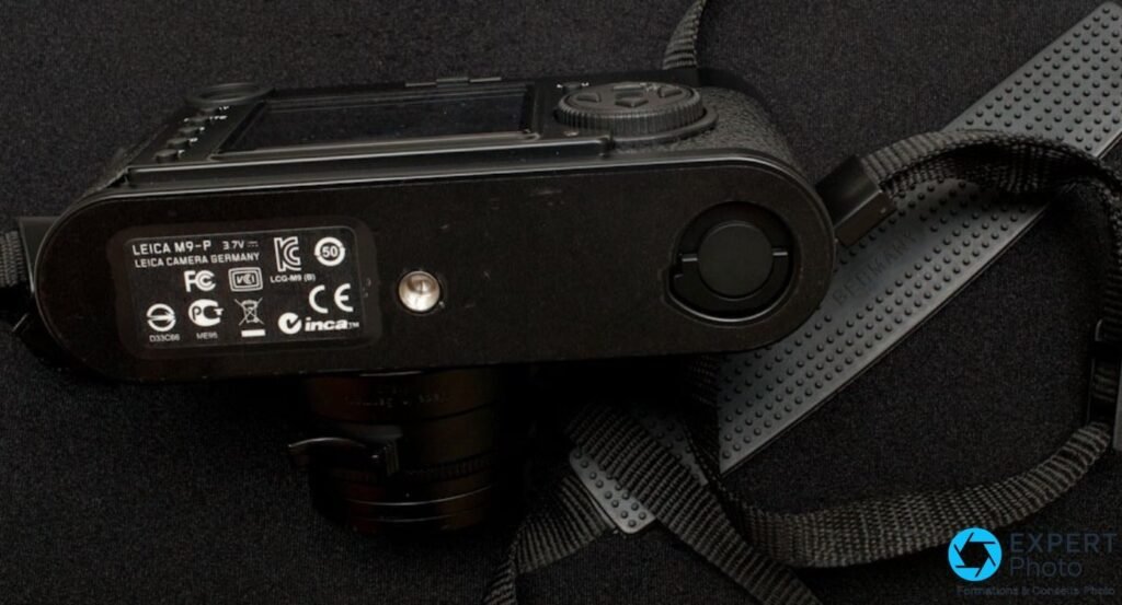 Dessous du Leica M9-P noir, plaque gravee Leica M9-P 3.7V, logos FCC CE KC et ecrou de trepied, sur fond noir