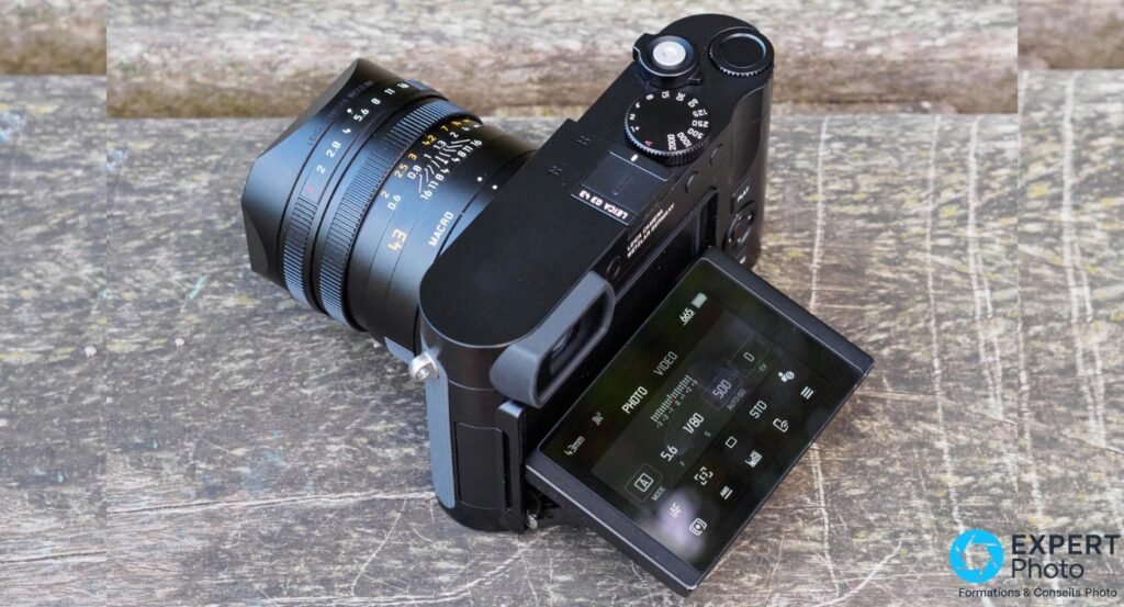  Leica Q3 43 noir, 3/4 arrière, écran incliné bas-angle, interface 43mm affichée, bagues objectif lisibles, fond bois
