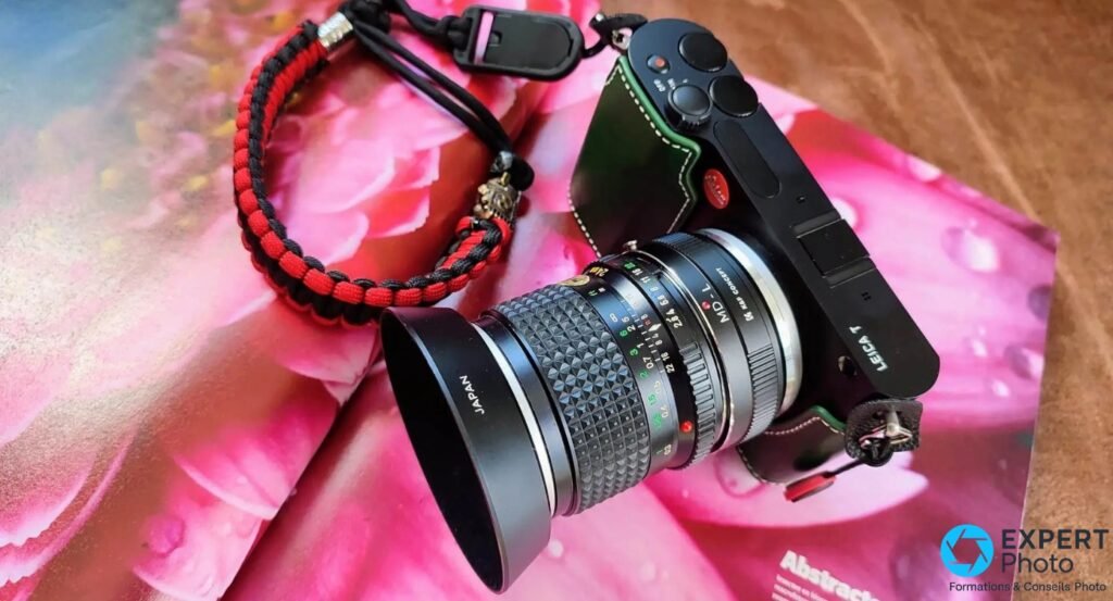 Leica T (Typ 701) avec objectif zoom adapté monté et pare-soleil marqué JAPAN, sangle tressée rouge et noire, sur fond rose